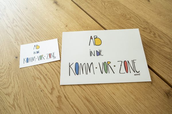 weiße Postkarte mit bunter Schrift "Ab in die Komm vor Zone"