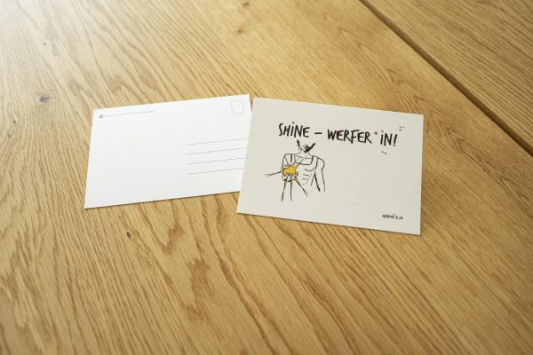 weiße Postkarte mit bunter Schrift "Shine-Werfer*in!"